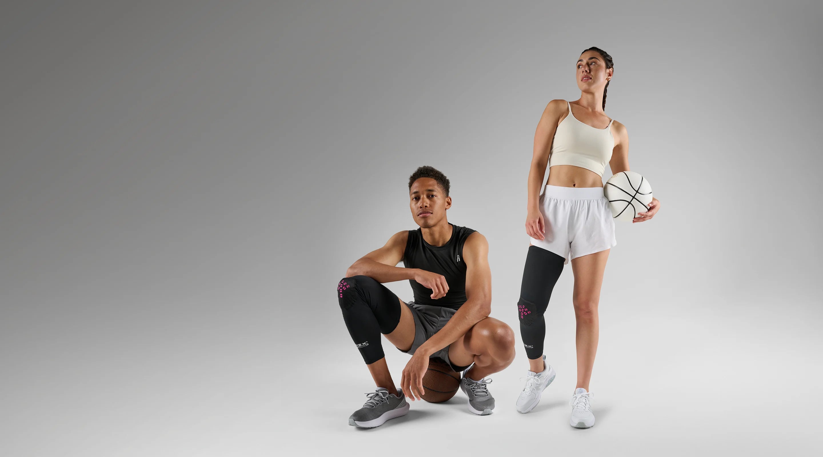 Two people in athletic wear with basketballs on a gray background