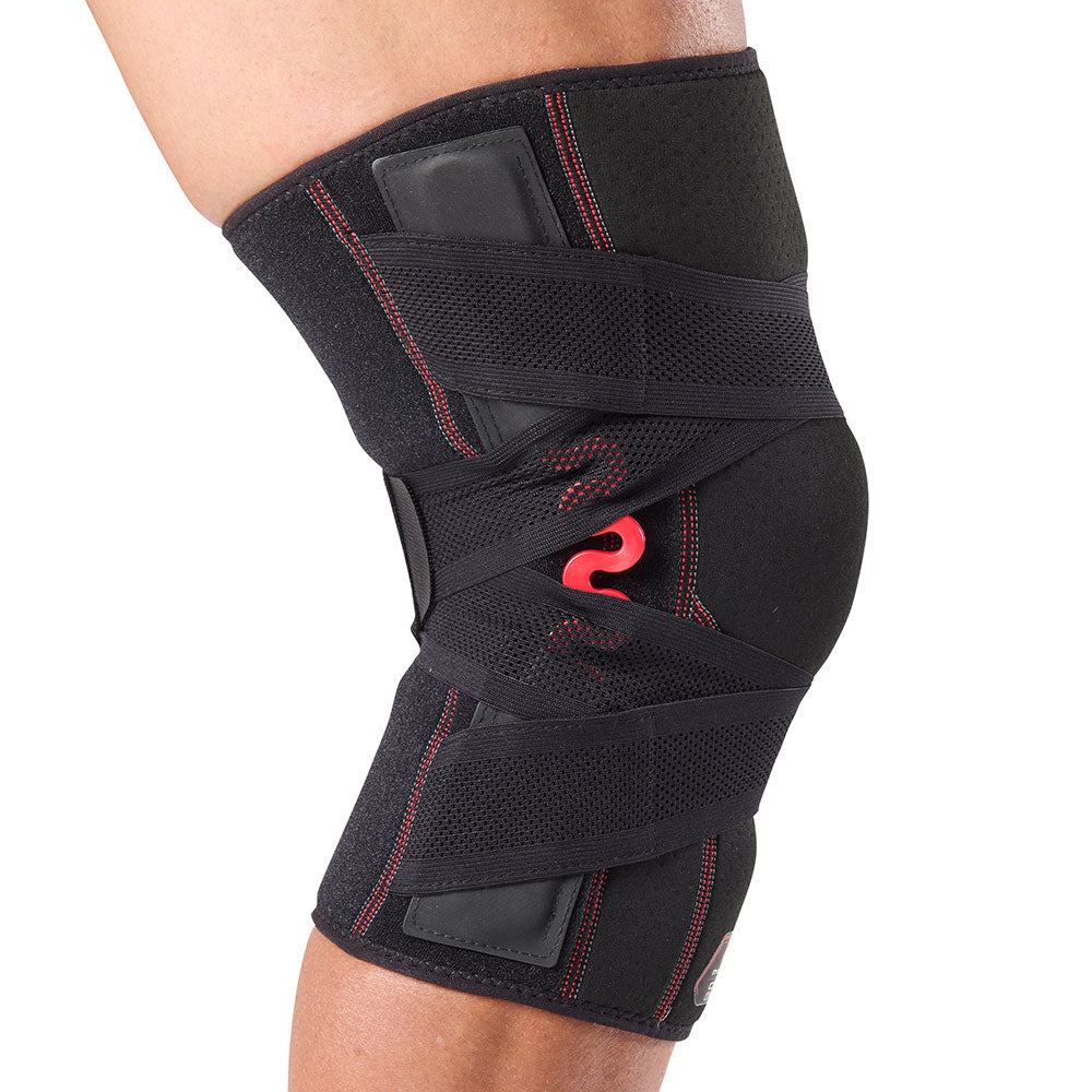 Side profile view of the McDavid NRG Cross Compression Knee Sleeve with Spring Hinge worn on a bent knee, highlighting the red spring hinge stabilizer along the side of the joint and the crossed compression strap configuration.