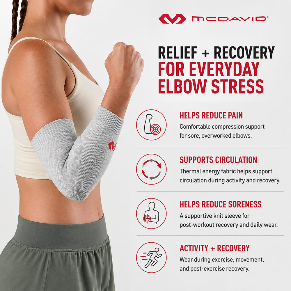 Woman flexing her arm while wearing the gray McDavid Infused Therapy elbow sleeve. The sleeve offers compression to help reduce pain and soreness, support circulation, and aid activity and recovery.